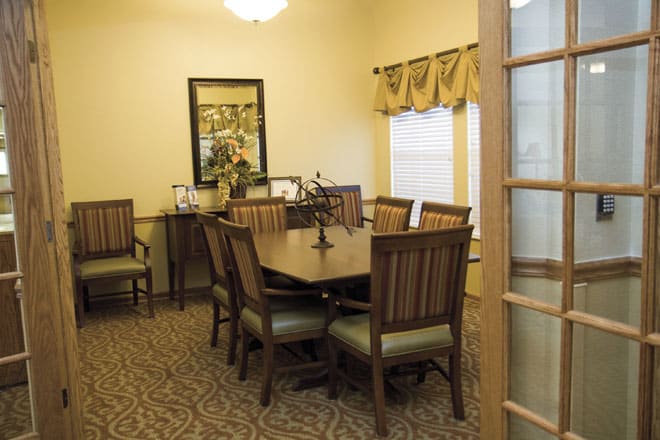 A neatly arranged dining room with a wooden table and chairs, featuring a mirror and window with drapes.