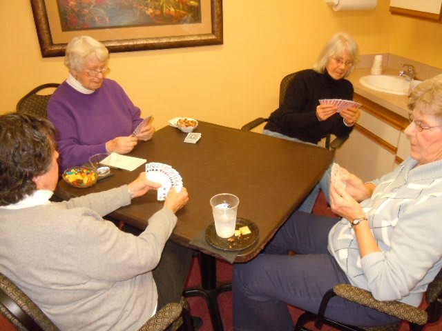 Four seniors gathered around a table playing a card game.