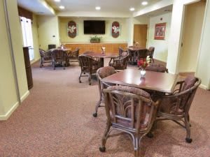 A cozy dining area with several tables and chairs, a TV mounted on the wall, and soft carpet flooring.