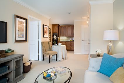 A cozy living space with neutral tones, featuring a seating area and a view into the kitchen.