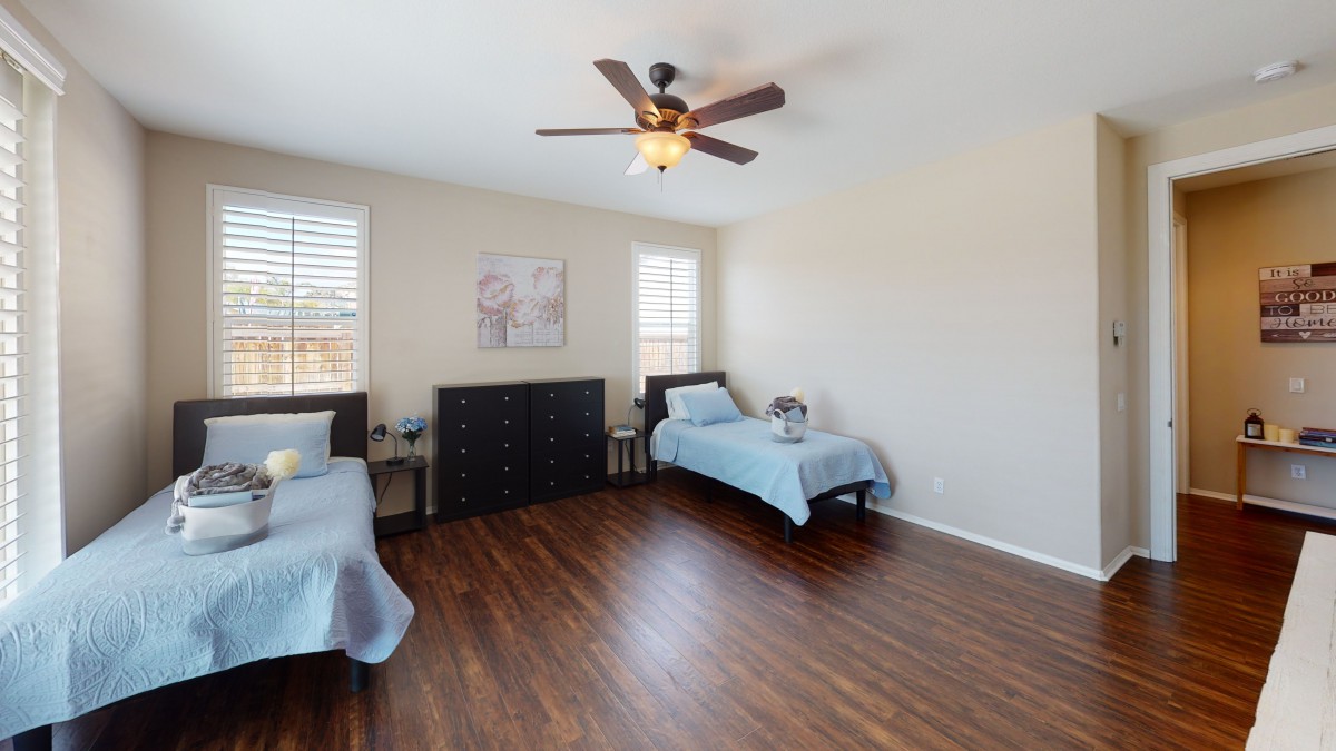 A minimalist bedroom featuring twin beds, hardwood flooring, and a ceiling fan.