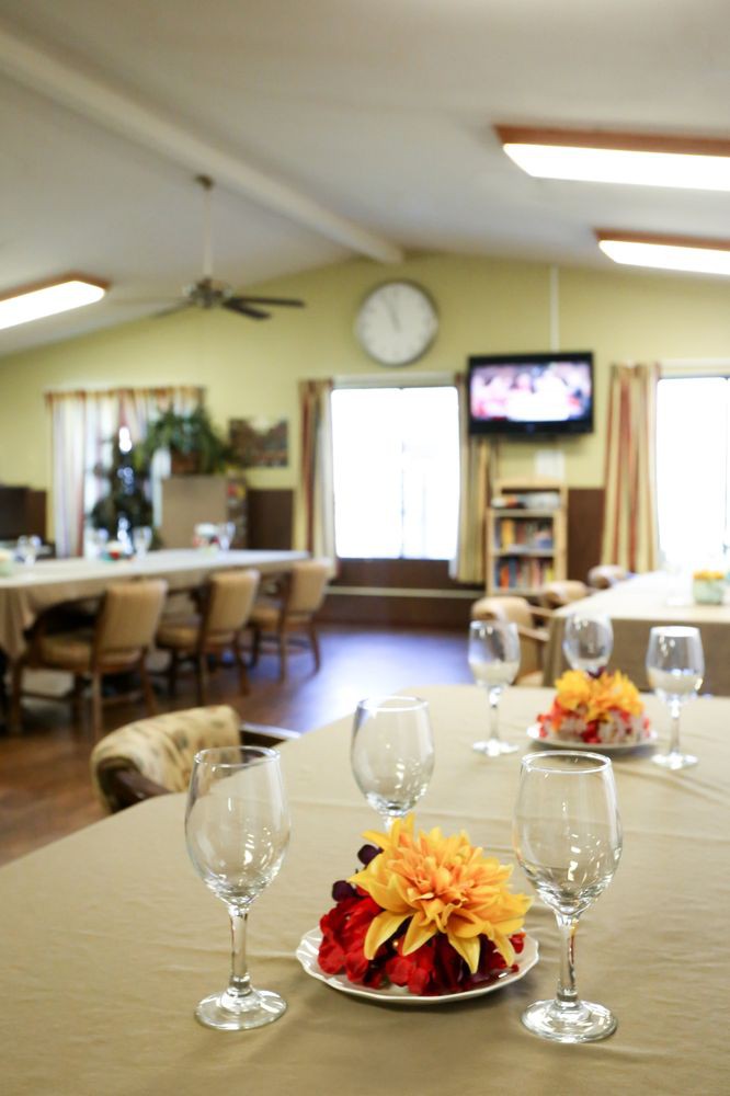 A dining room with tables set for an event, featuring elegant glassware and floral centerpieces, with a television in the background.