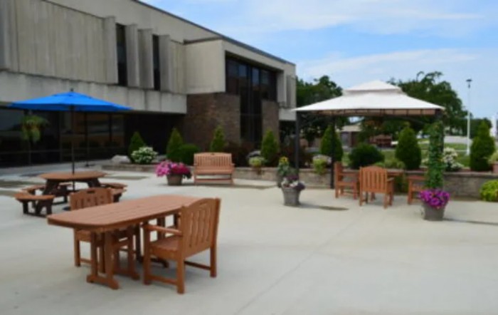 An outdoor patio area featuring wooden tables and chairs, large umbrellas, and potted plants.