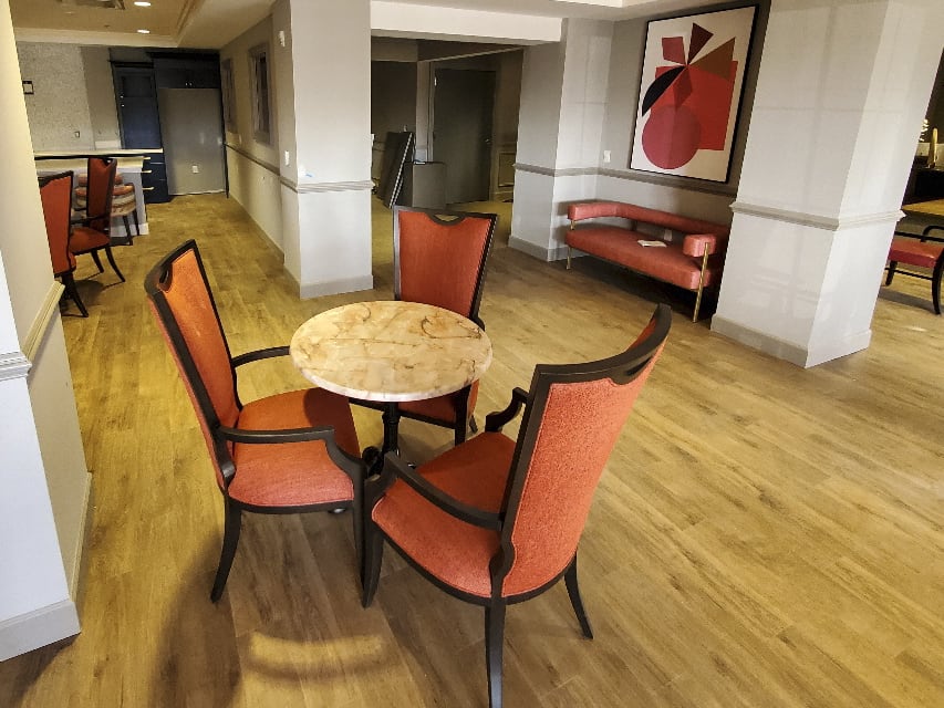 A cozy lounge area featuring a round table with four orange chairs and abstract artwork on the wall.