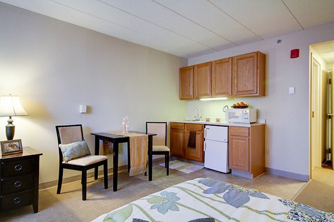 A cozy studio apartment featuring a compact kitchenette with wooden cabinets, a small dining table with two chairs, and simple interior decor.
