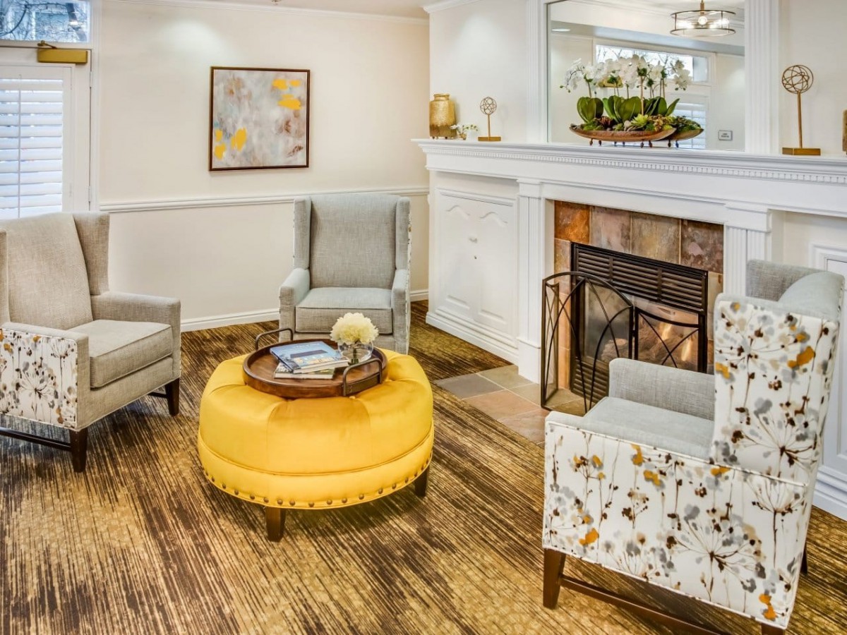 A cozy living room with a fireplace, featuring comfortable armchairs and a bright yellow ottoman.
