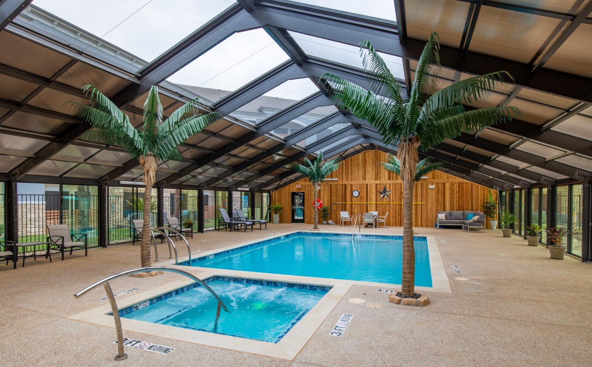 An inviting indoor swimming pool with a glass roof and palm trees, perfect for relaxation.