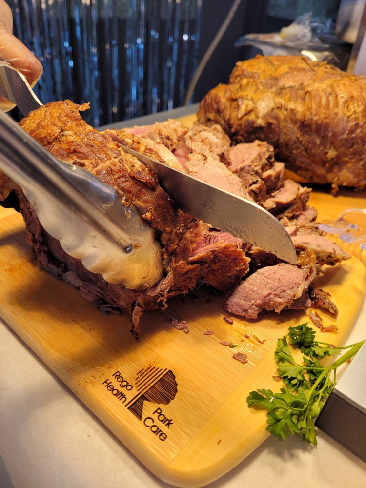A chef carves a piece of roasted meat on a wooden cutting board.