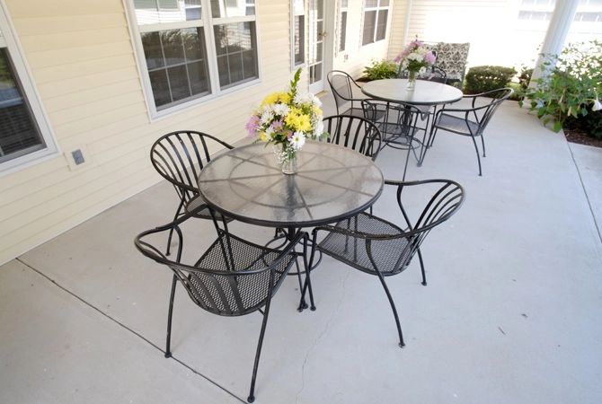 A patio with metal tables and chairs, featuring floral centerpieces.