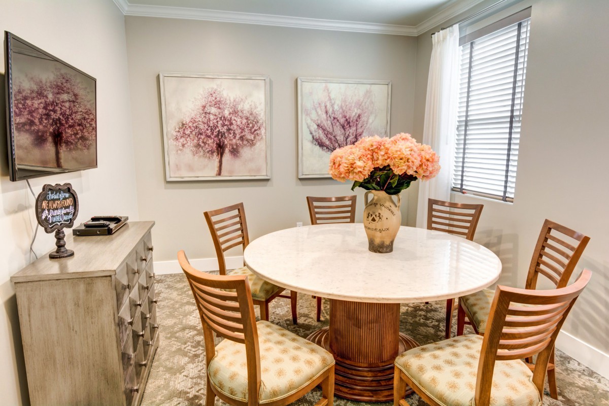A cozy dining room featuring a round table with a floral centerpiece and decorative wall art.