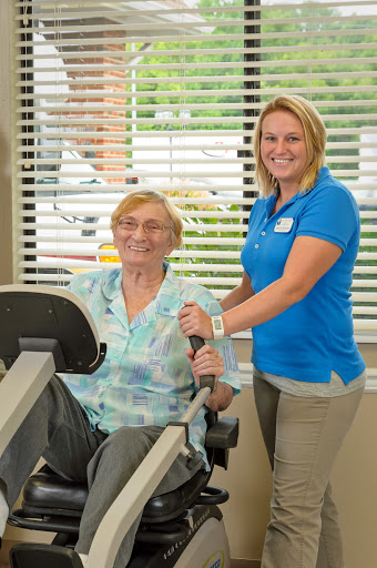 A personal trainer assists a senior client during a workout session in a rehabilitative fitness environment.