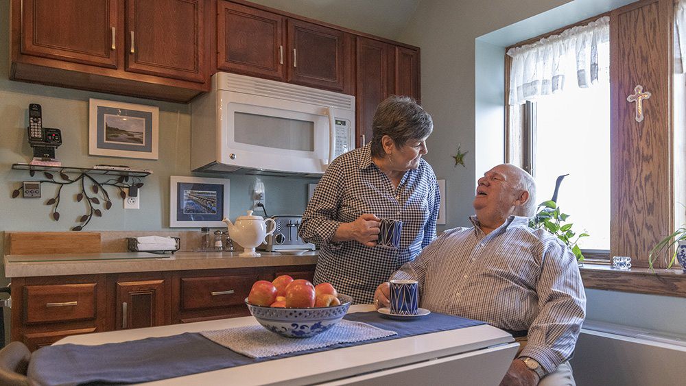 An elderly couple enjoying a conversation over coffee in their kitchen.