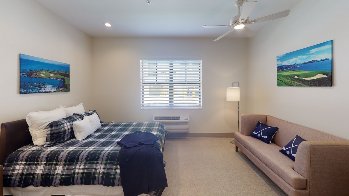 A cozy bedroom with a bed, couch, and lamp by the window.