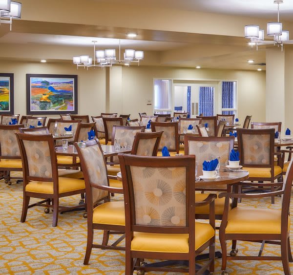 A spacious dining area with neatly arranged tables and chairs, featuring elegant chandeliers and modern decor.