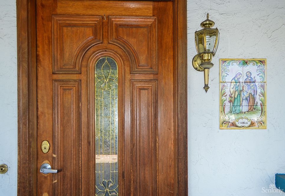 A wooden front door with stained glass, accompanied by a wall-mounted lantern and decorative artwork.