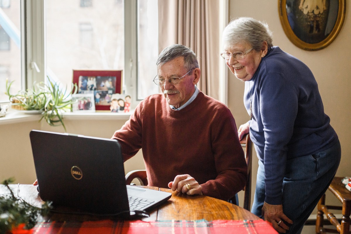 Two senior individuals are using a laptop together at home.