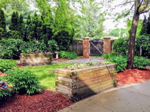 A beautifully landscaped garden with wooden planters, lush greenery, and a pathway leading to a wooden gate.