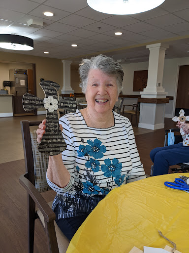 A joyful senior woman proudly displaying her handmade cross during a crafting activity.