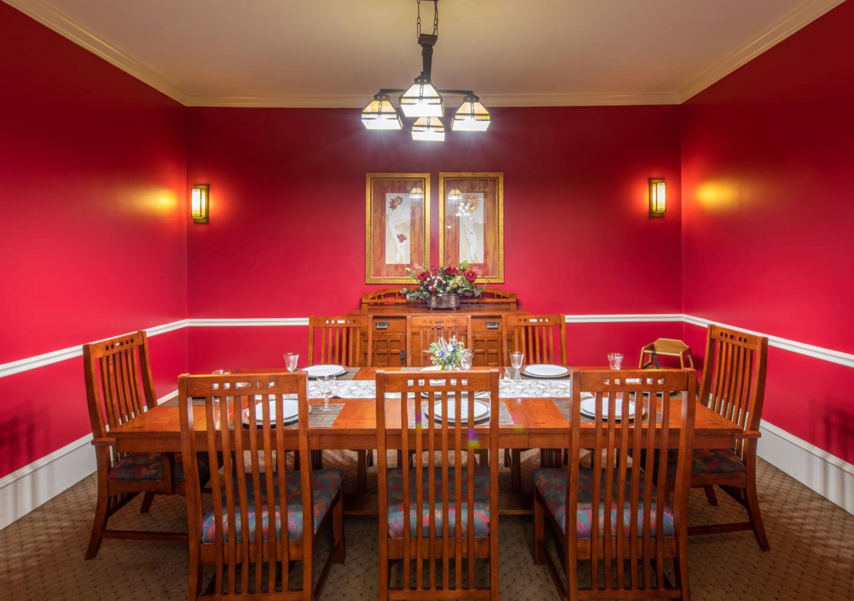 A formal dining room with wooden furniture and red walls, featuring a chandelier and decorative lighting.