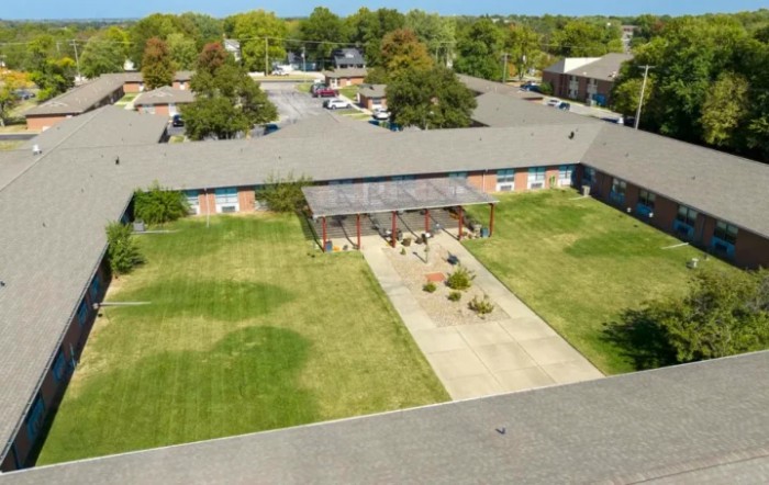 Aerial view of a single-story building with a central driveway, surrounded by grass and trees.