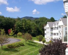 A scenic view of a white building surrounded by lush greenery, with mountains in the background.