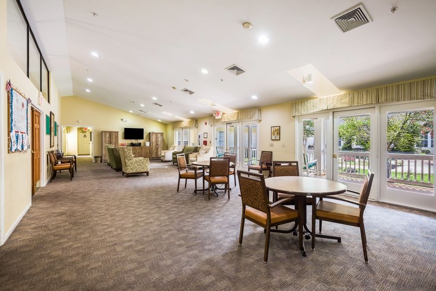 A spacious and well-lit living area with multiple tables and chairs, featuring large windows and a comfortable atmosphere.