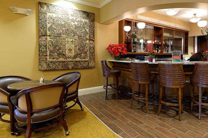 A cozy bar interior with wooden chairs, a counter, and a decorative tapestry on the wall.