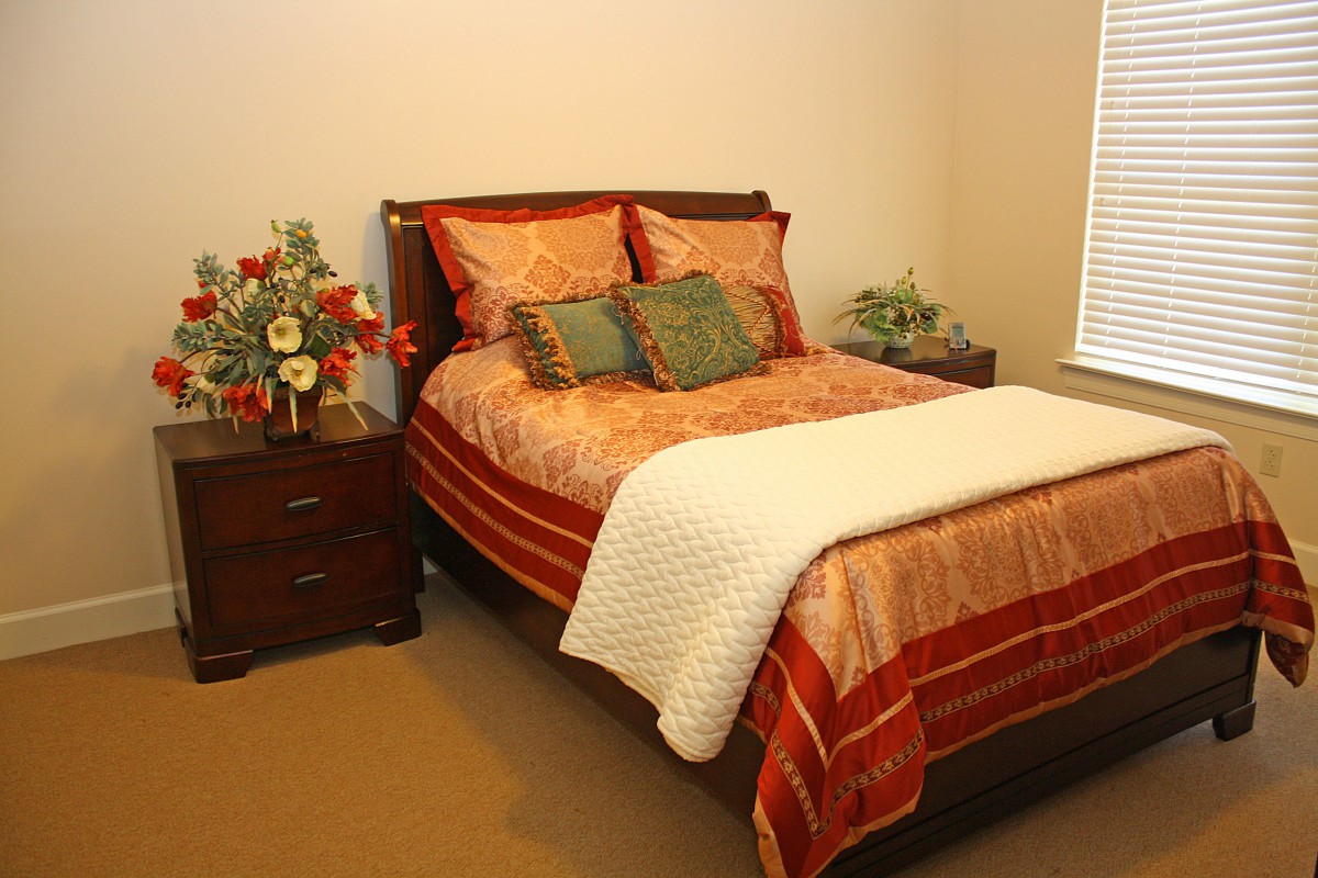 A cozy bedroom featuring a bed with elegant bedding and decorative pillows, accompanied by wooden nightstands with lamps and floral arrangements.