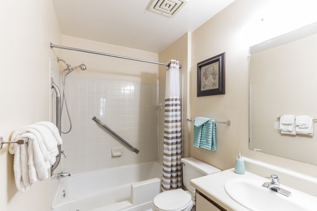 A clean and minimalistic bathroom with a bathtub, shower curtain, sink, and neatly arranged towels.