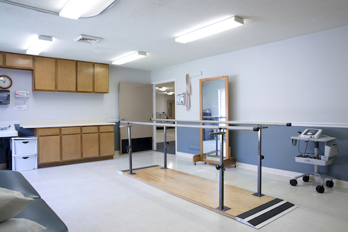 A spacious physical therapy room equipped with a barre for rehabilitation exercises.
