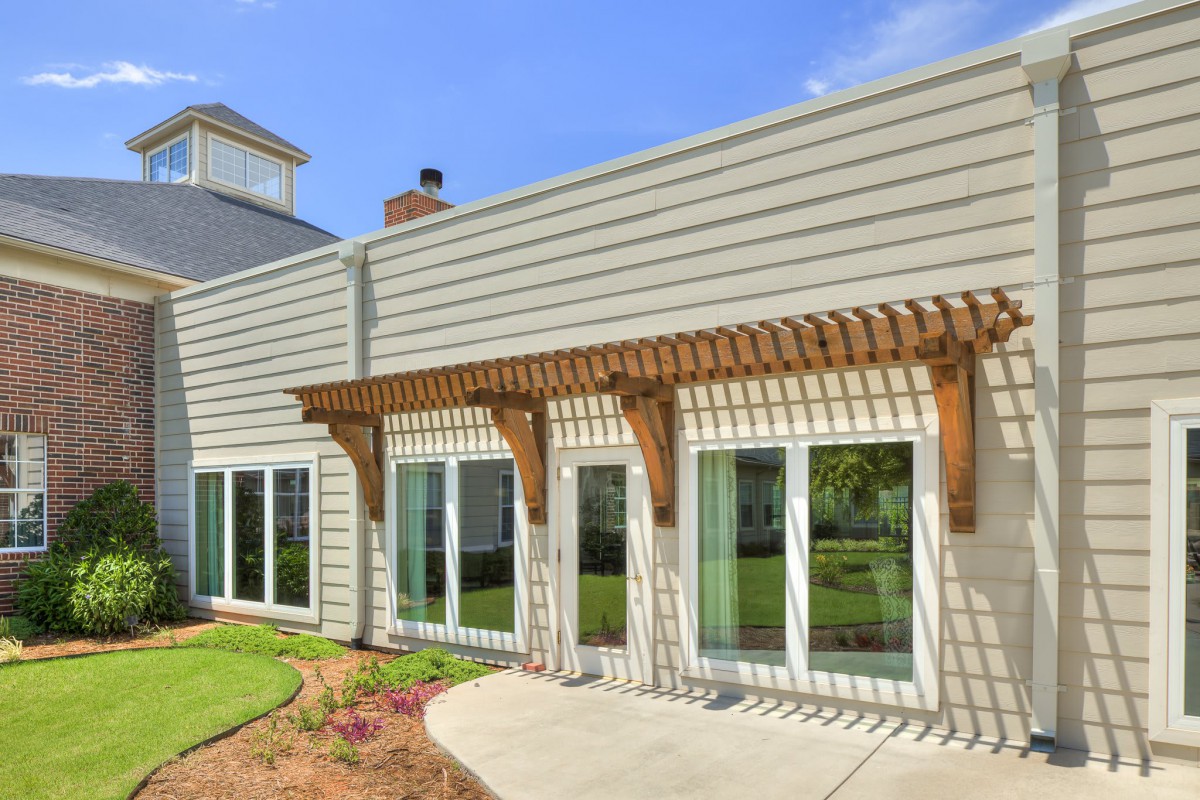 A modern house exterior with a pergola structure over the patio and large glass windows.