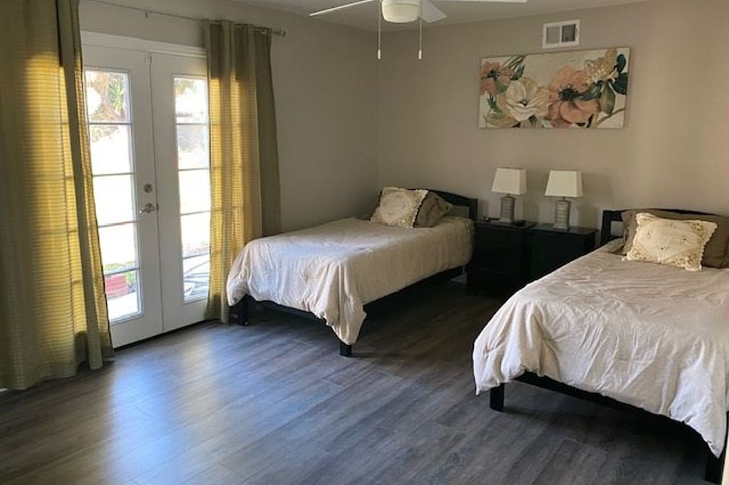 A modern bedroom featuring twin beds, French doors, and stylish decor.