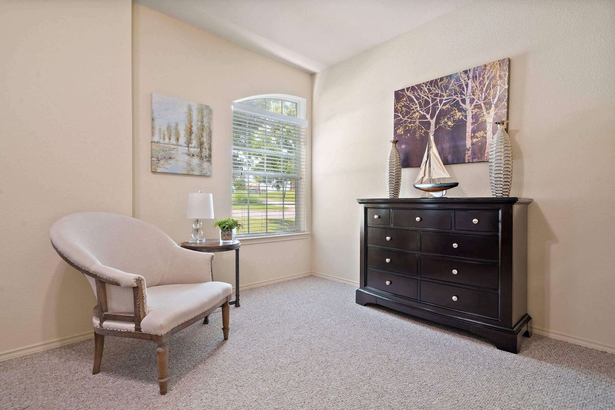 A cozy living room with a comfortable chair, a dresser, and large windows letting in natural light.