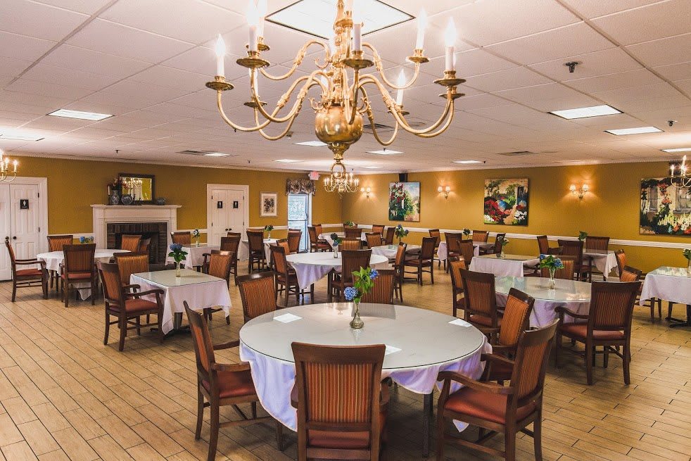 An elegant dining room with a central chandelier, round tables, and comfortable chairs.