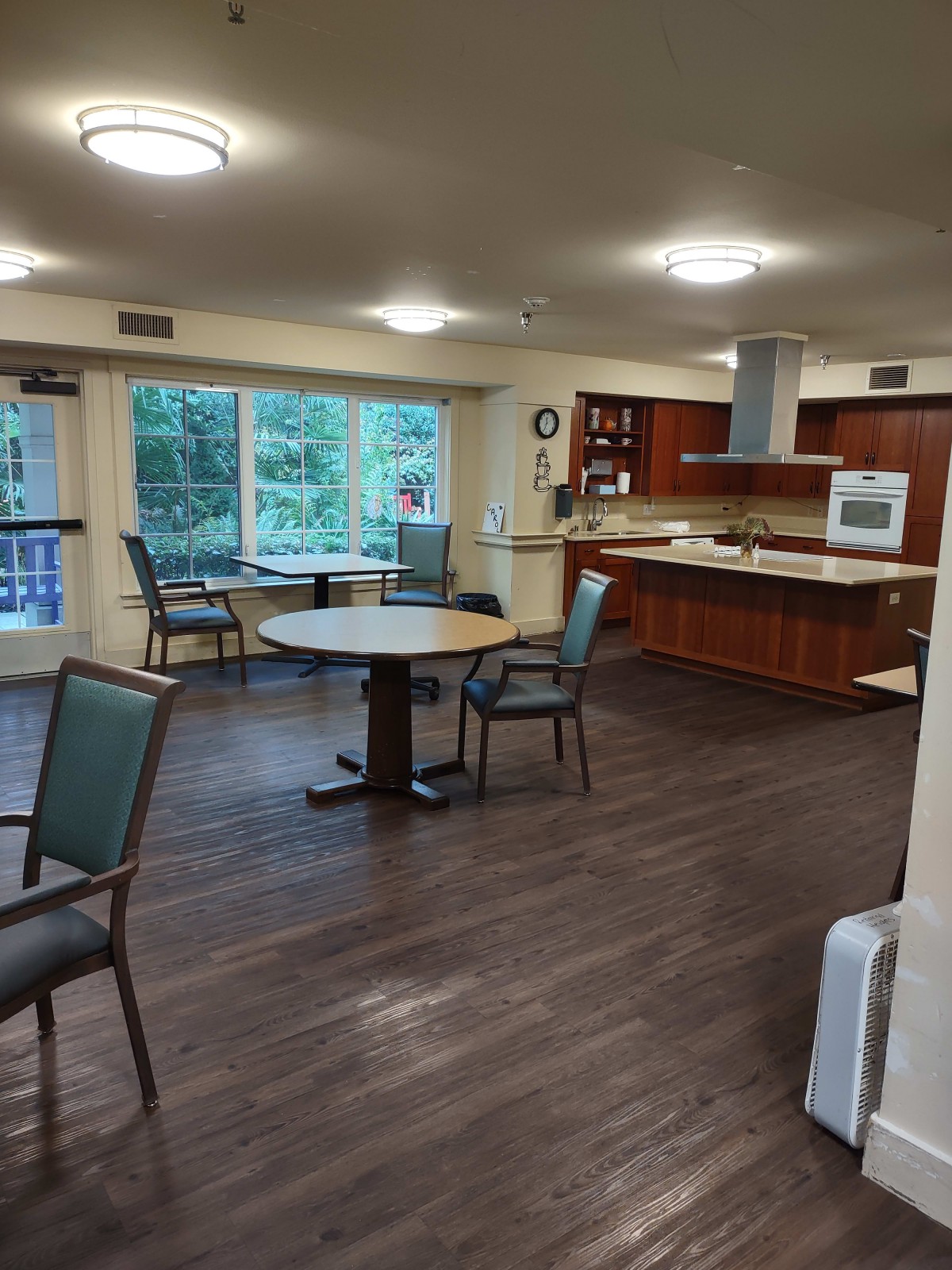 An open dining and kitchen area with wood flooring, featuring a table and chairs with large windows letting in natural light.