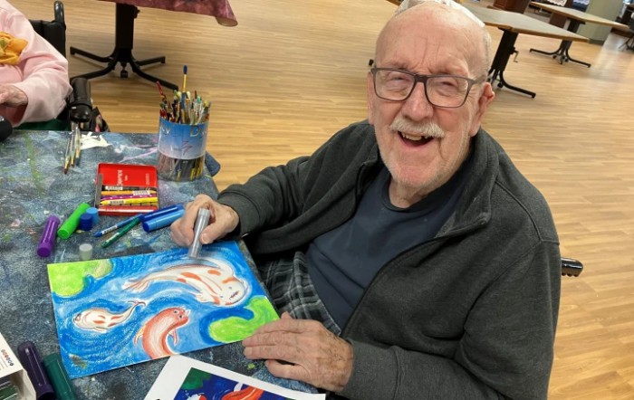 An elderly person happily creating a colorful painting indoors.