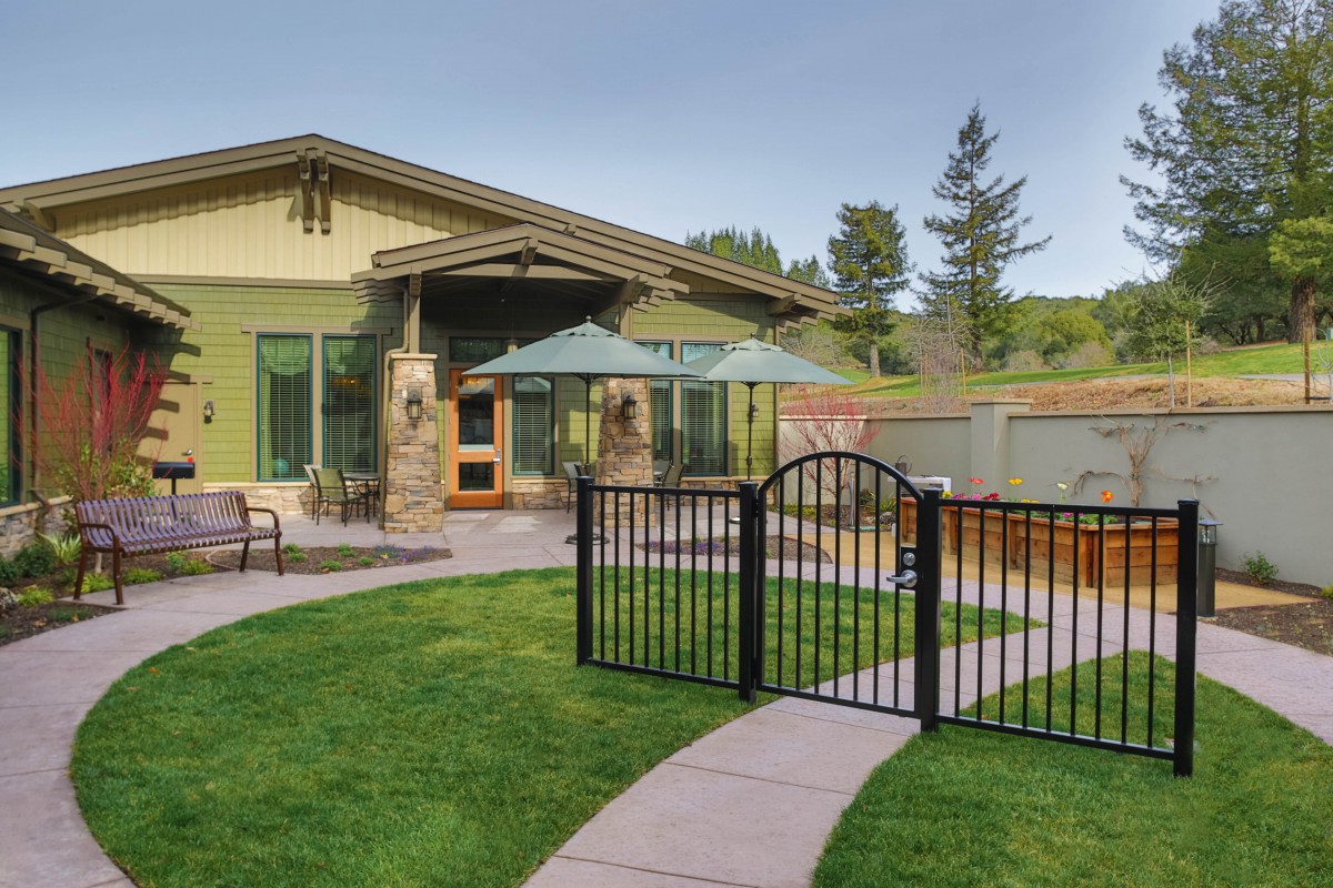 A modern patio and garden area with a small gate, lawn, and outdoor furniture.
