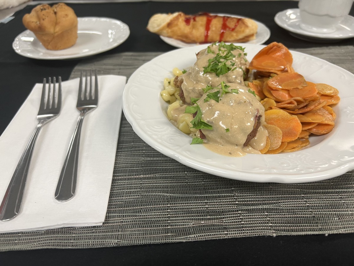 A plated meal consisting of meatballs with gravy and vegetables, accompanied by a bread roll and muffin.