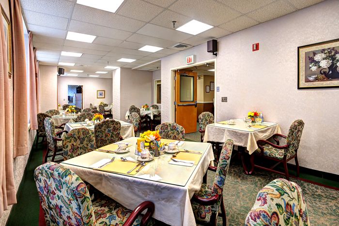 A well-lit dining room with tables set for a meal, featuring floral decorations and patterned chairs.