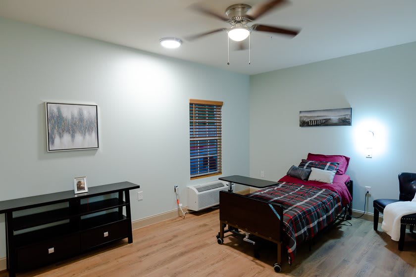 A simple bedroom with a hospital bed, featuring minimalist decor and wooden flooring.