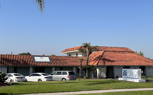A residential house featuring a red tile roof and palm trees under a clear blue sky.