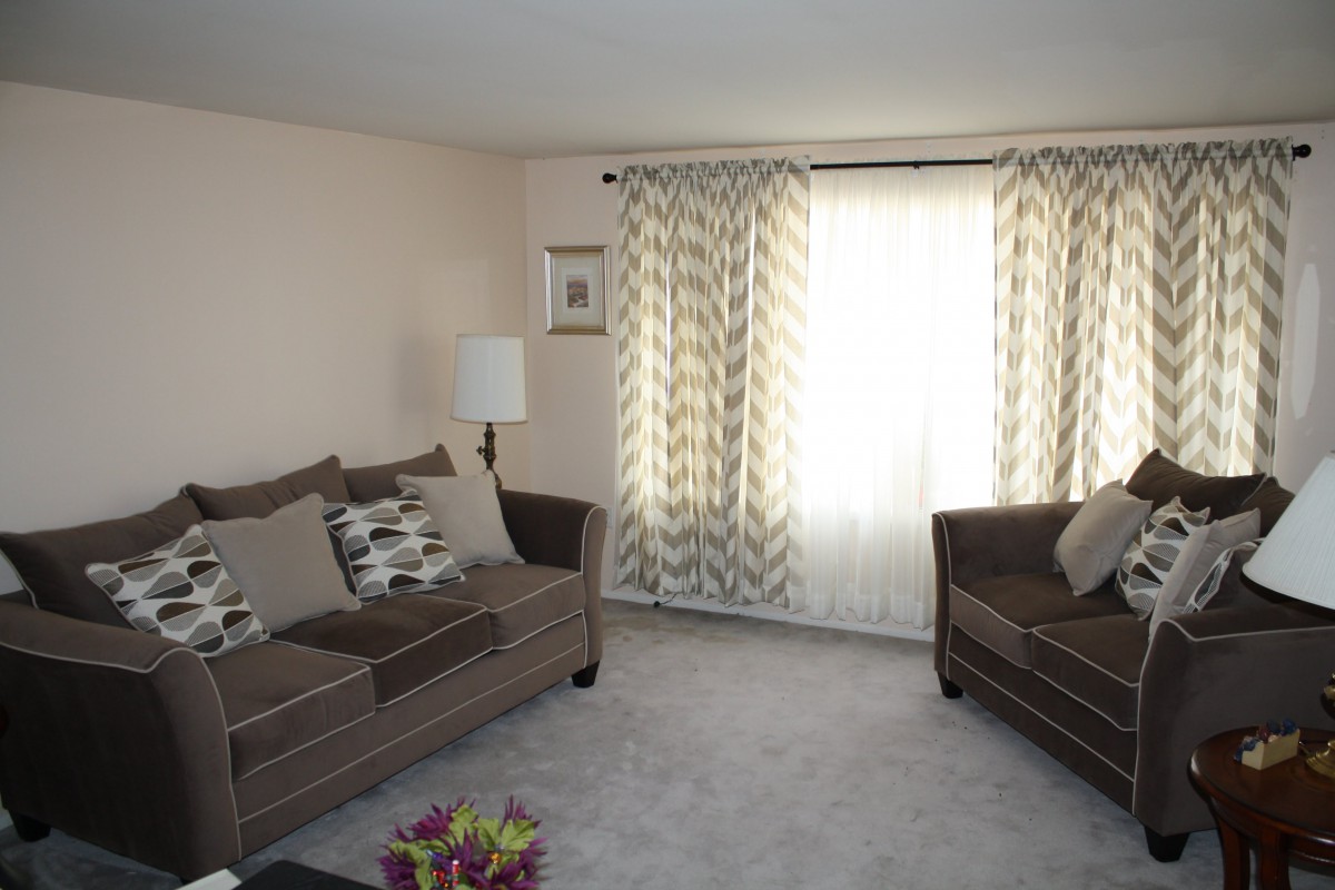A cozy living room with two sofas, patterned curtains, and a lamp.