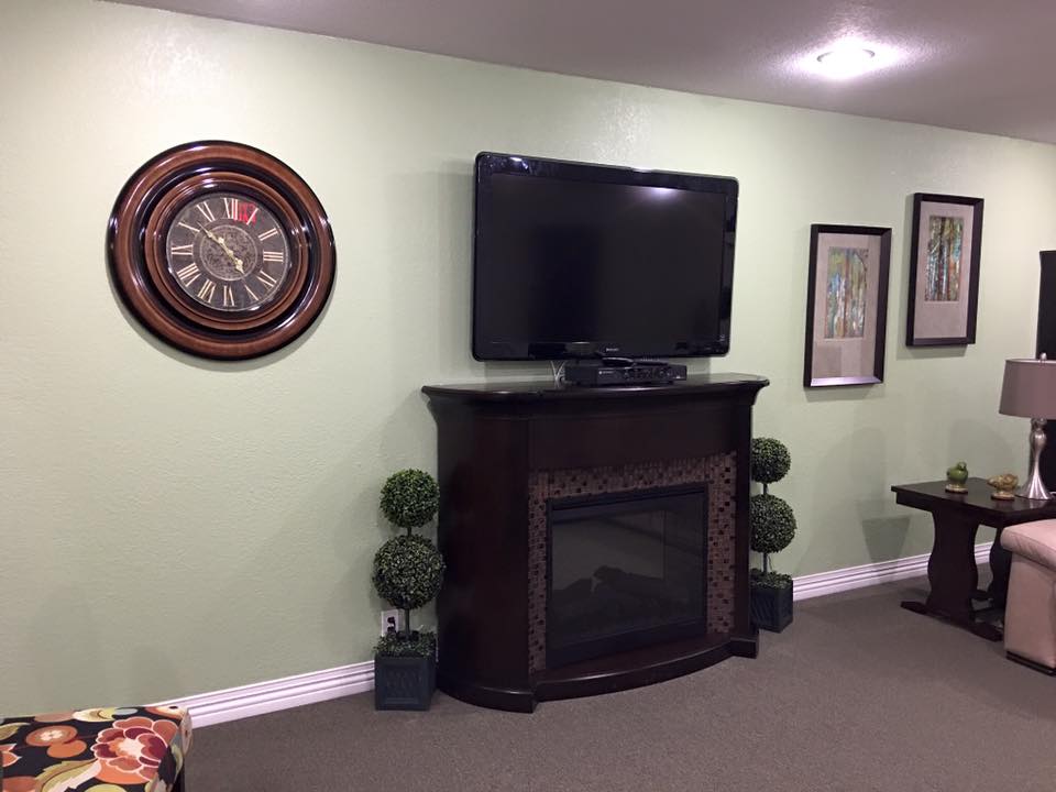 A cozy living room with a wall-mounted television above a fireplace, accompanied by a decorative clock and framed pictures.