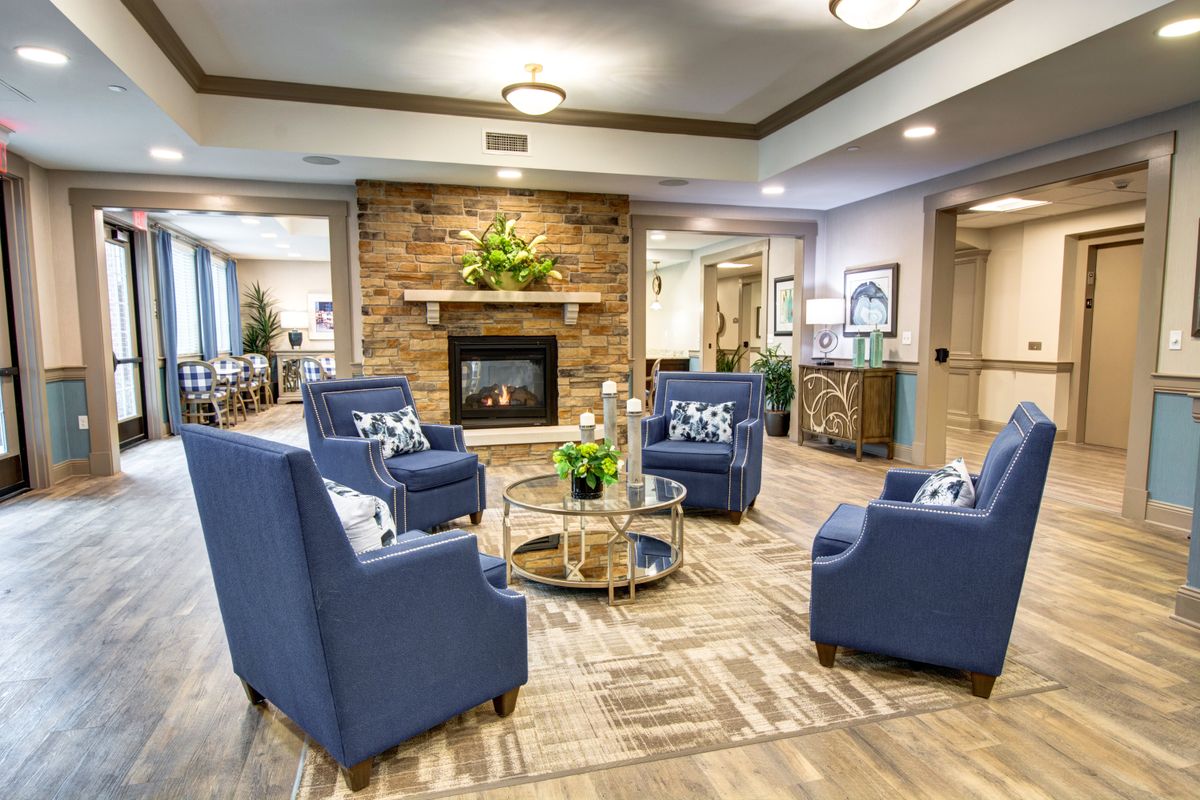 A cozy living room with blue armchairs arranged around a glass coffee table and a stone fireplace.