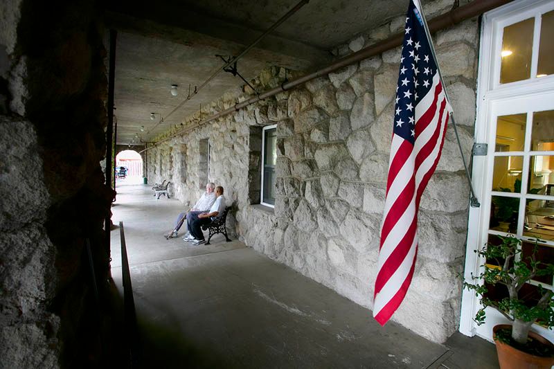 A corridor with a stone wall featuring an American flag and two people sitting on a bench.