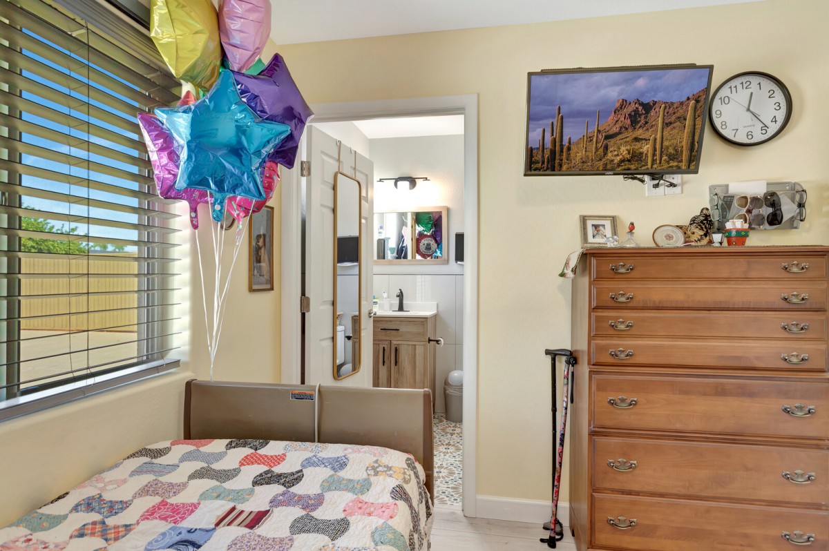 A cozy bedroom with colorful balloons above the bed, a wooden dresser, and an open doorway leading to a bathroom.