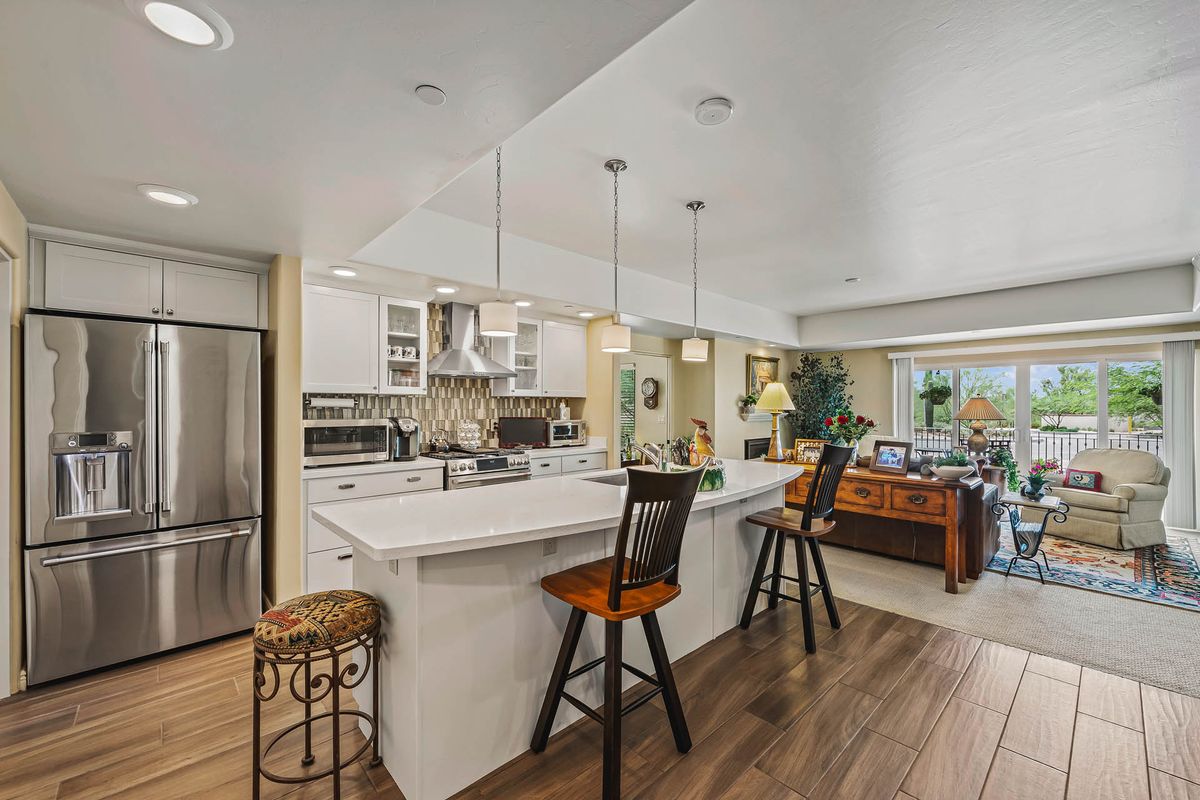 A modern kitchen interior featuring an island with barstools, pendant lighting, and white cabinetry, complemented by wood flooring.