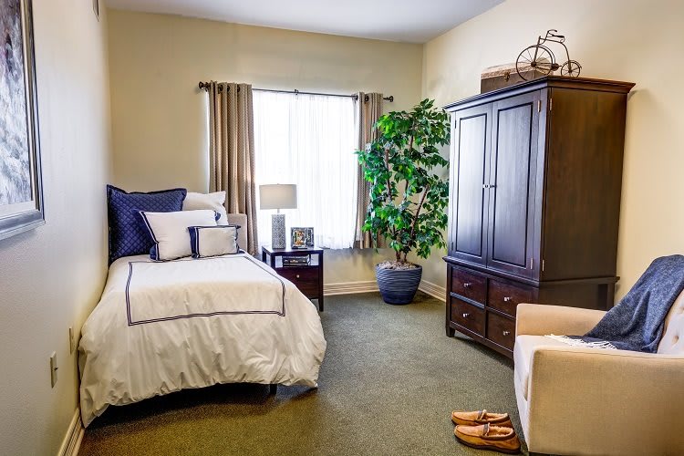 A cozy bedroom with a neatly made bed, a wooden wardrobe, and a potted plant by the window.