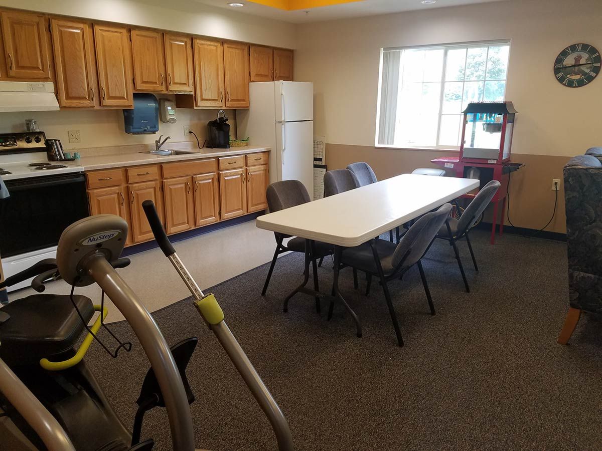 A multi-purpose room with a kitchen area, table and chairs, exercise equipment, and a popcorn machine.