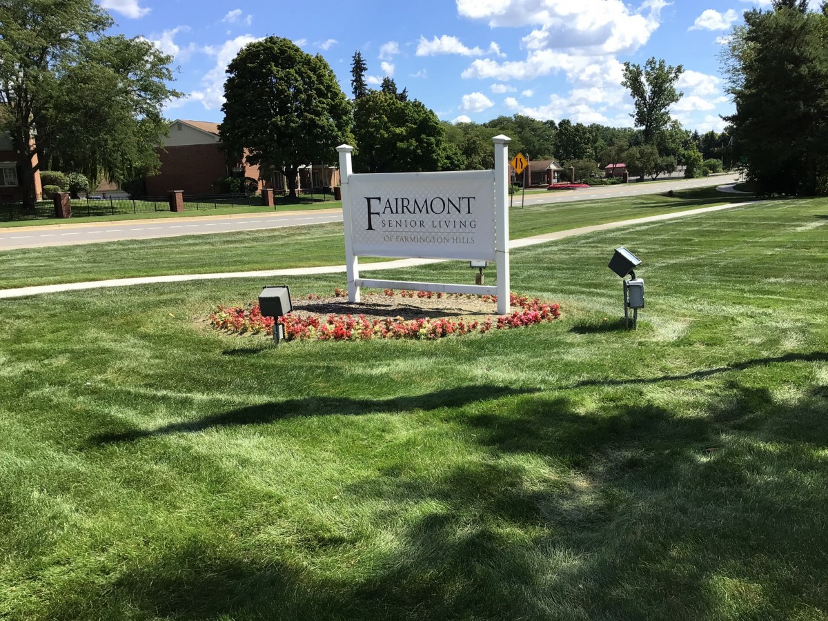 A landscaped entrance with a sign for Fairmont featuring flowers and well-maintained grass.